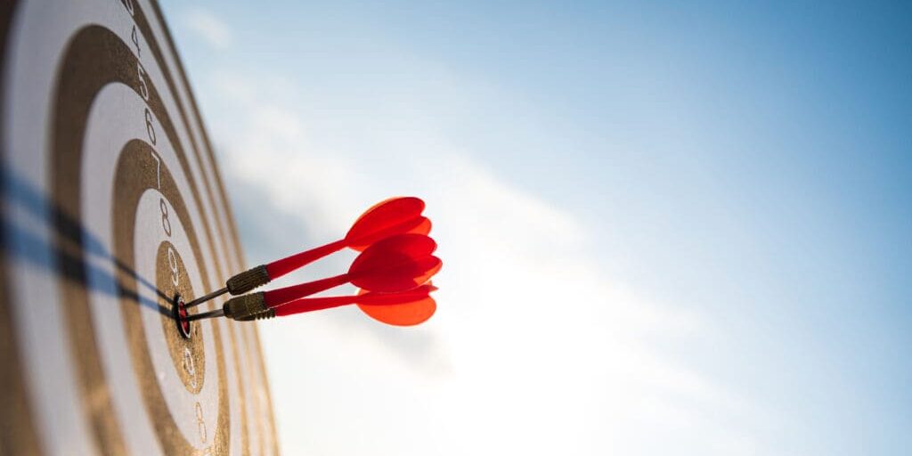 Close up shot red darts arrows in the target center on dark blue sky background. Business target or goal success and winner concept.